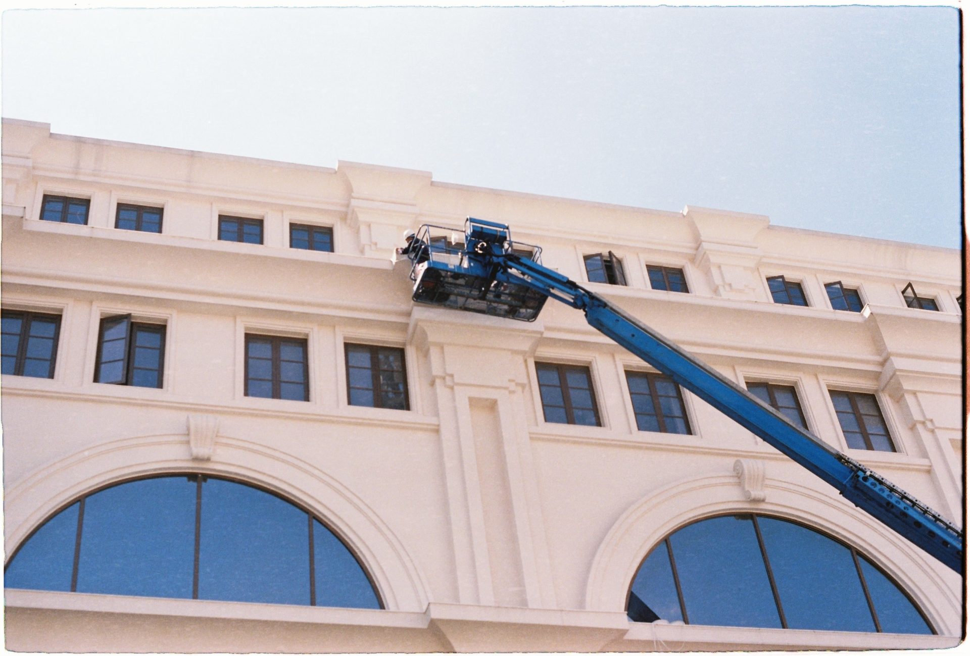 Par temps clair, un ouvrier nettoie les vitres d'un immeuble à l'aide d'une grue bleue.
