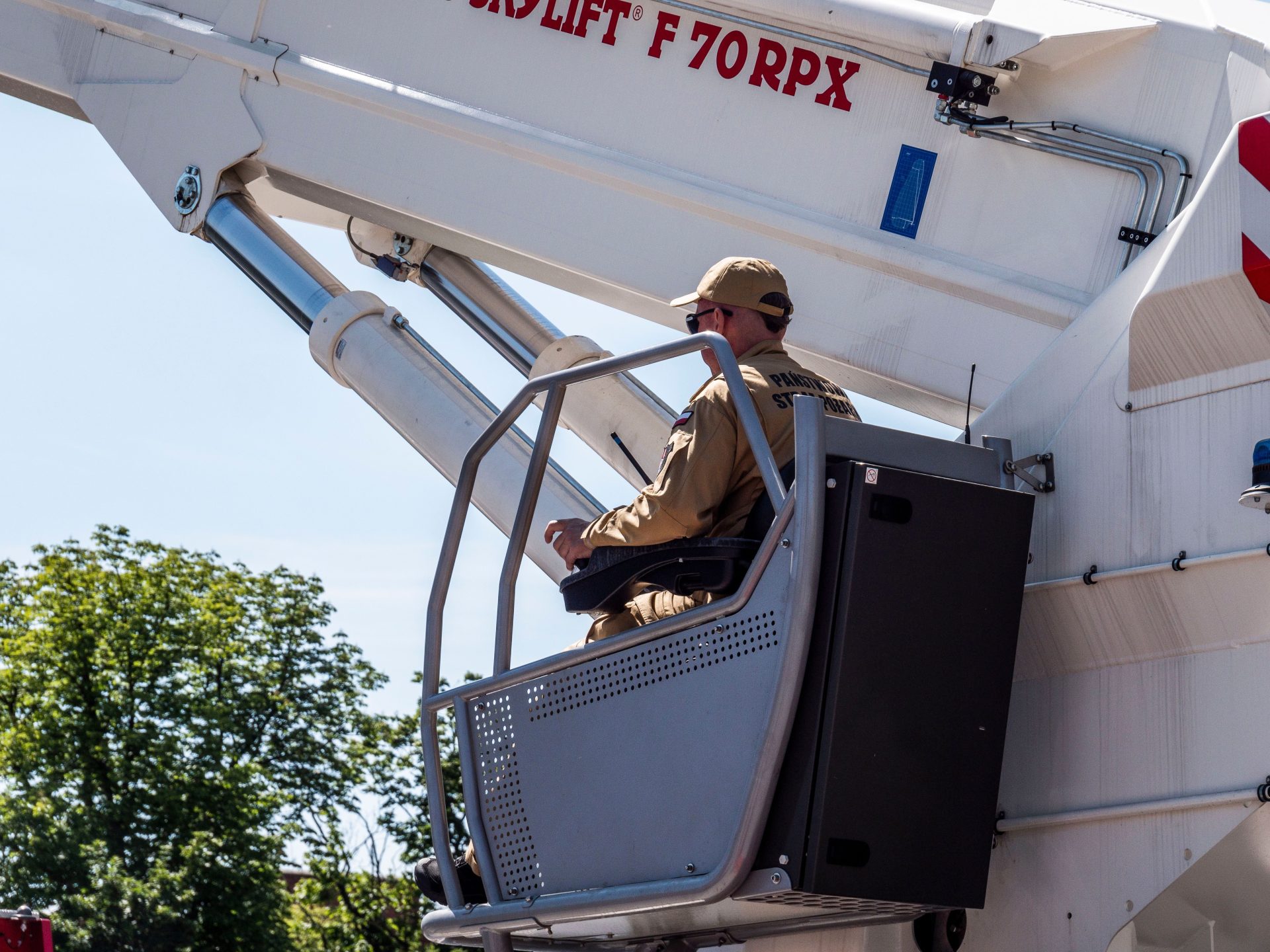 Un ouvrier en uniforme manœuvre une nacelle élévatrice à grande portée à l'extérieur par une journée ensoleillée.